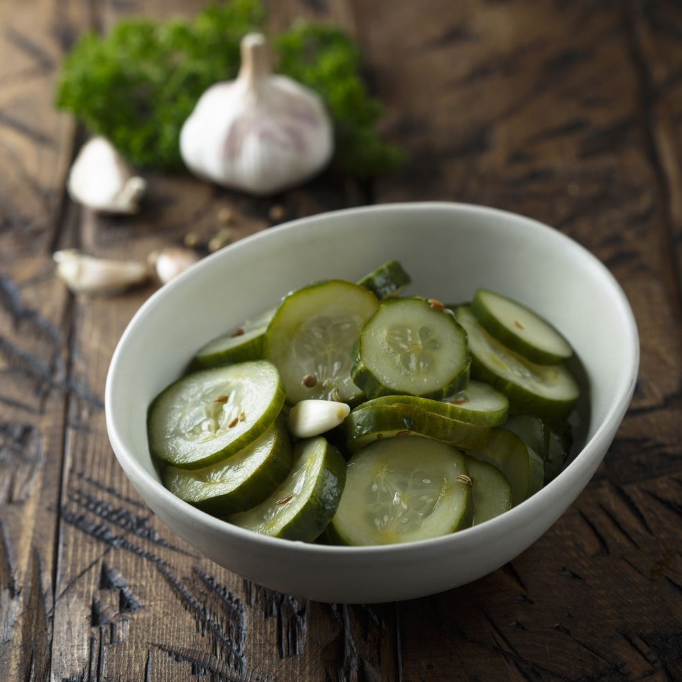 a white bowl of pickled cucumbers on a wooden tabletop
