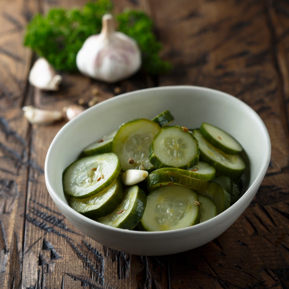 a white bowl of pickled cucumbers on a wooden tabletop