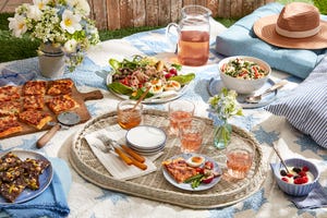 picnic foods, including flatbread, salad, and glasses of rose on a blanket