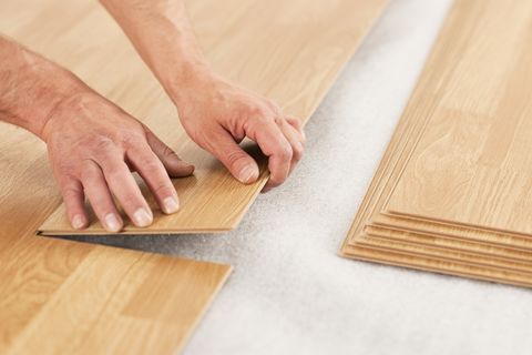 Picture of man's hands laying yellow laminate flooring