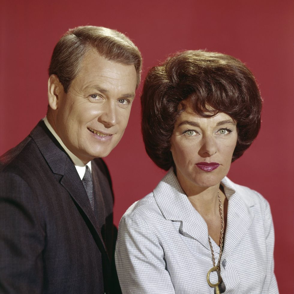 bob barker and dorothy jo gideon look directly at the camera, standing in front of a red wall