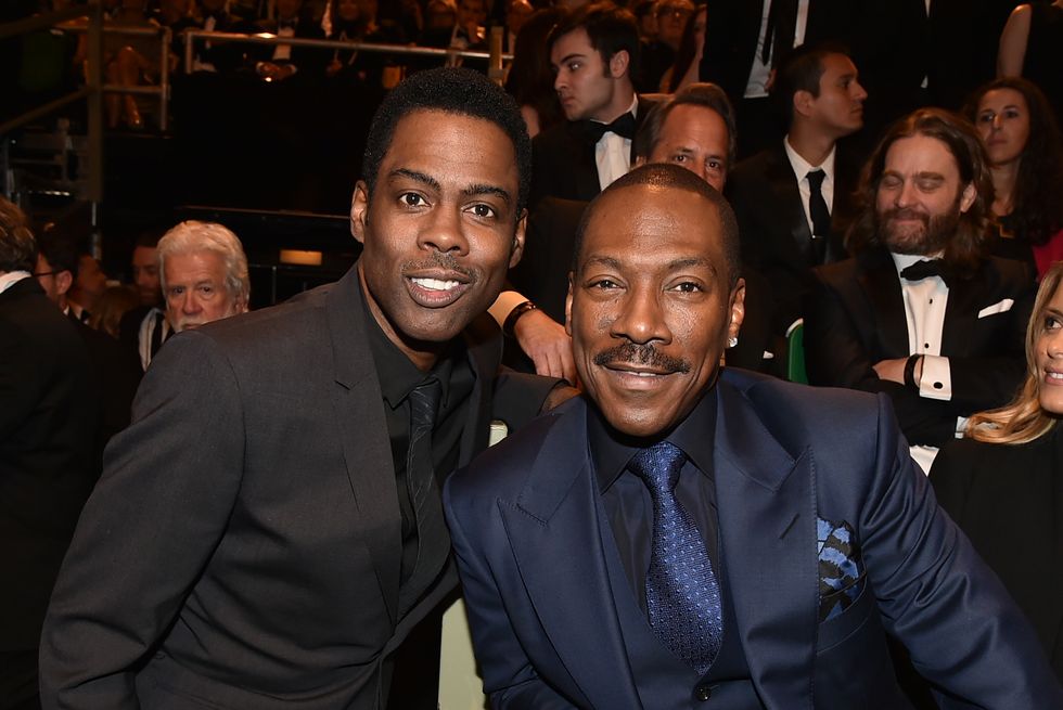 chris rock and eddie murphy in a crowded room, smiling at the camera and wearing black suits