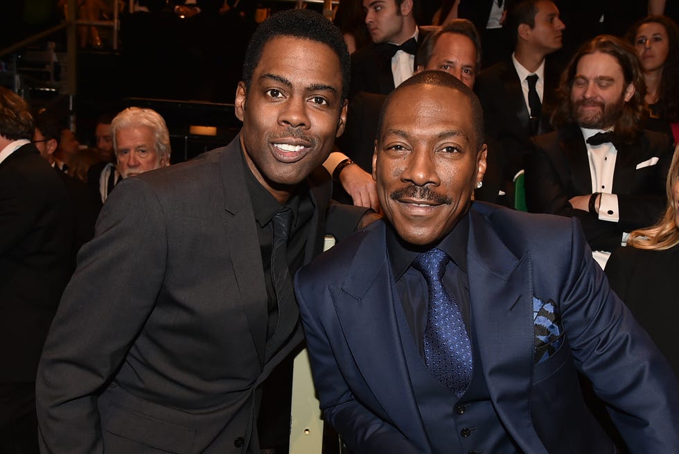 chris rock and eddie murphy in a crowded room, smiling at the camera and wearing black suits