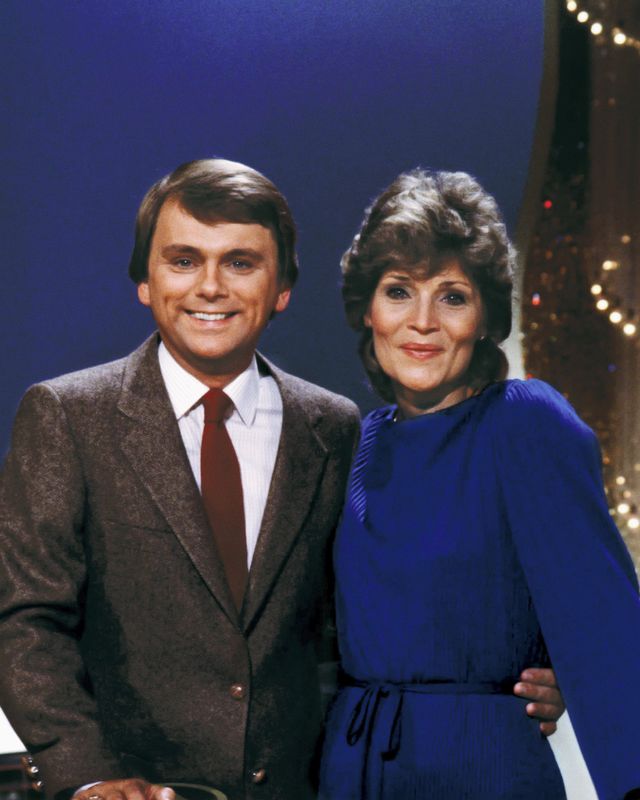 pat sajak and susan stafford embracing behind the wheel of fortune hosting lectern