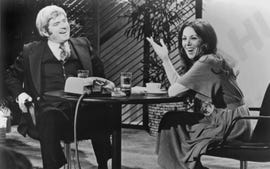 phil donahue sitting on the left side of a table with a telephone on it and smiling as marlo thomas gestures on the opposite side