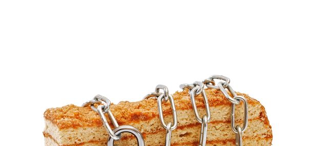 piece of layered honey cake isolated wrapped by chain and locked with padlock on white background