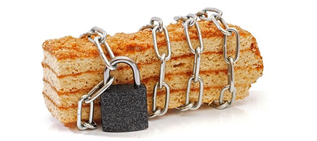 piece of layered honey cake isolated wrapped by chain and locked with padlock on white background