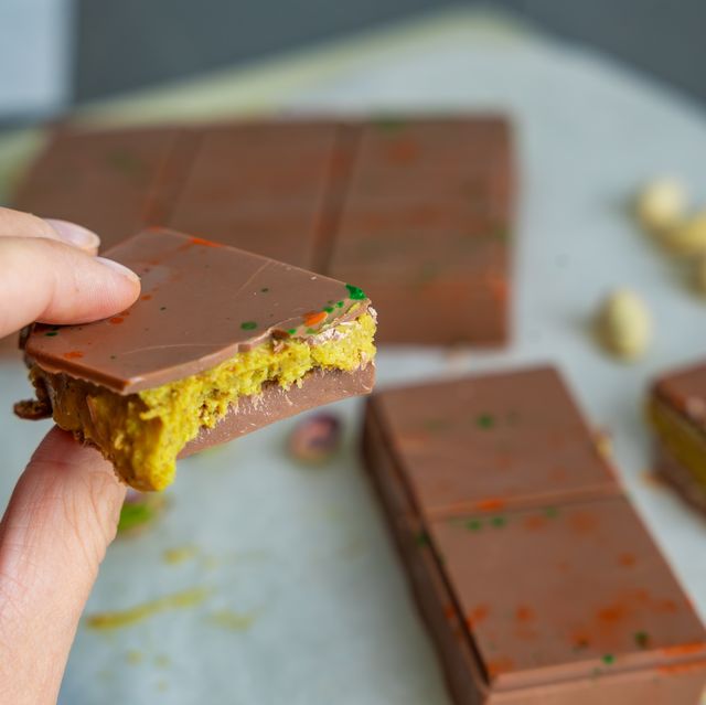 piece of trend dubai chocolate with pistachio paste and kataifi dough in woman hand. confectionery handmade sweets at home in the kitchen.