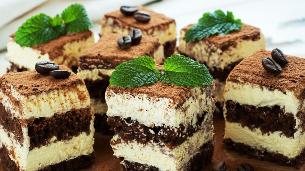 pieces of tiramisu cake with delicate cream, coffee beans and mint leaves