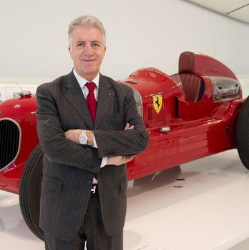 piero ferrari standing in front of a vintage ferrari race car at a museum