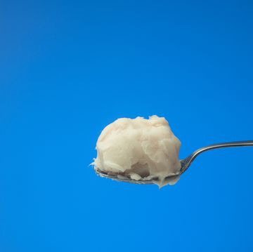 pig fat or lard on a metal spoon held by caucasian male hand close up studio shot, isolated on blue background