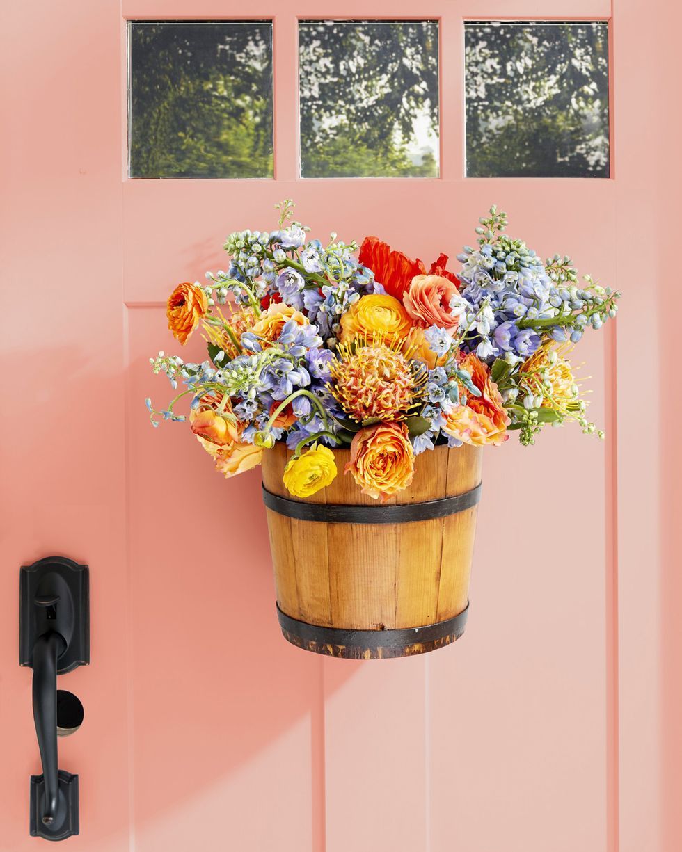 a piggin bucket hung on a pink door and filled with loads of purple, orange, and red summer flowers