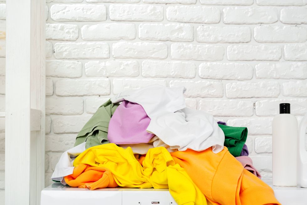 pile of laundry awaiting washing machine in white brick laundry room