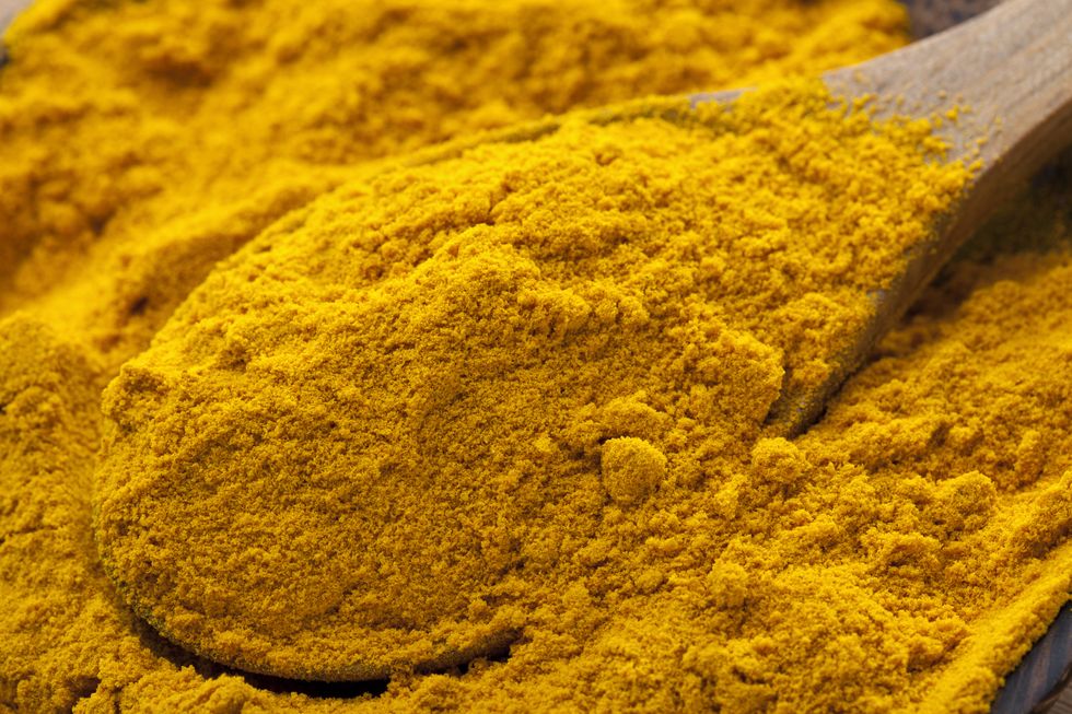 A pile of turmeric in a bowl with a wooden spoon