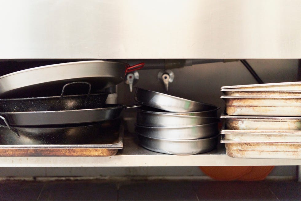 piles of pans and containers stacked in a row in some kitchen cabinets in a restaurant kitchen, front close up view