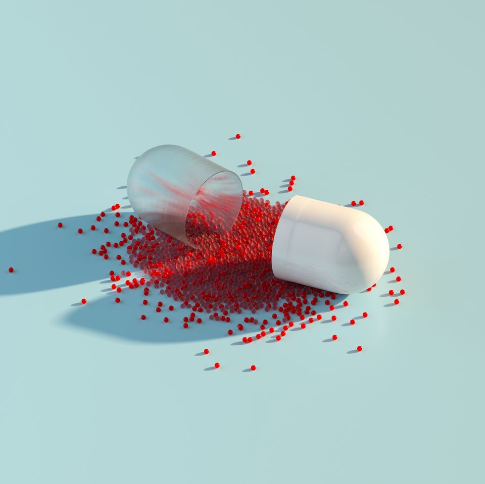 digital generated image of abstract opened plastic capsule pill with small red spheres inside on pastel blue background