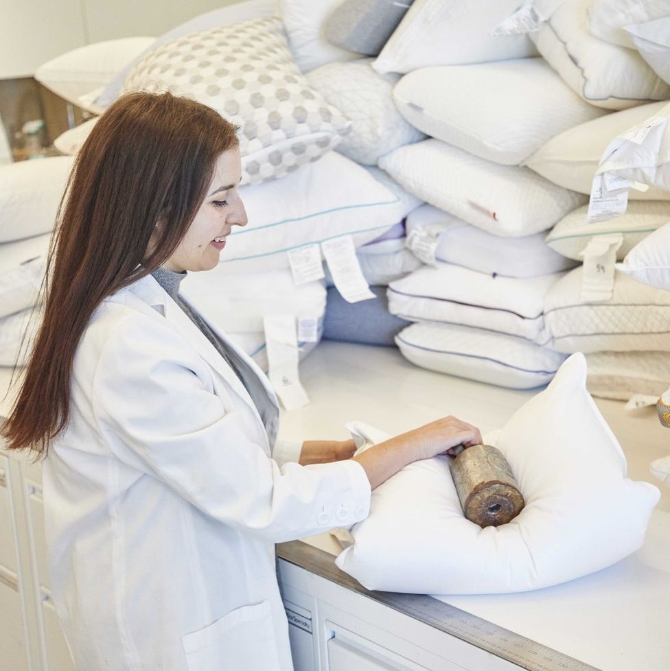 a good housekeeping analyst putting a weight on a folded down pillow, good housekeeping's testing for best down pillows