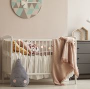 pillows and toy in white wooden crib with pastel pink blanket in bright nursery