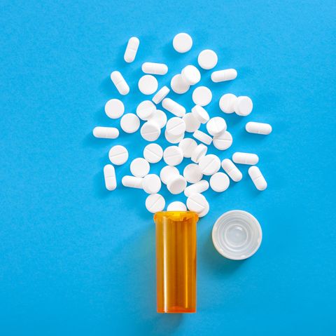 Pills falling from pill bottle on blue background with copyspace