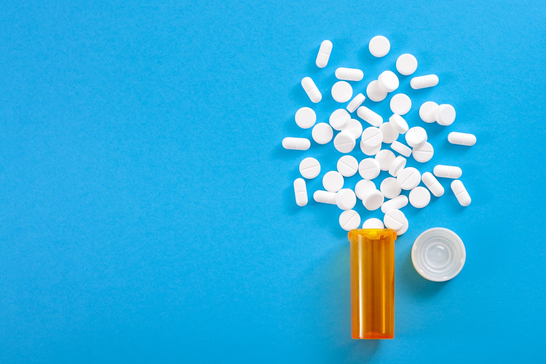 pills falling from pill bottle on blue background with copyspace