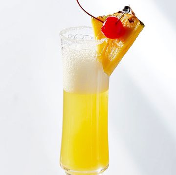 yellow bubbly drink in a champagne glass garnished with a pineapple wedge and maraschino cherry