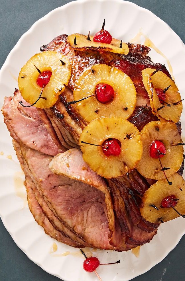 brown sugar glazed ham with pineapple rings stuck through with maraschino cherries on a white plate