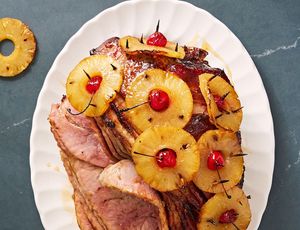 brown sugar glazed ham with pineapple rings stuck through with maraschino cherries on a white plate