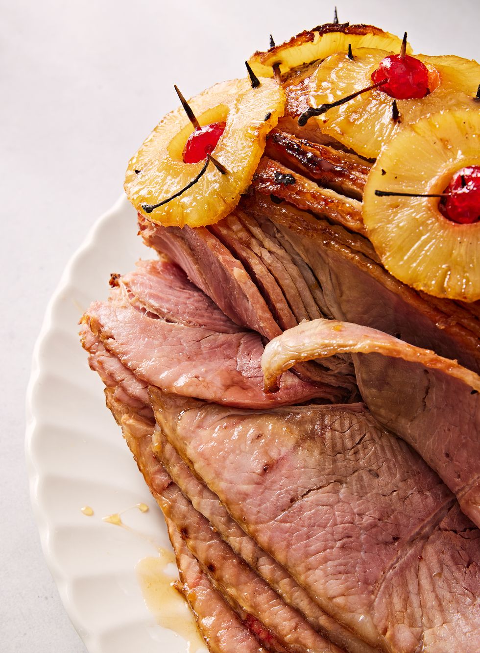 close up of brown sugar glazed ham with pineapple rings stuck through with maraschino cherries