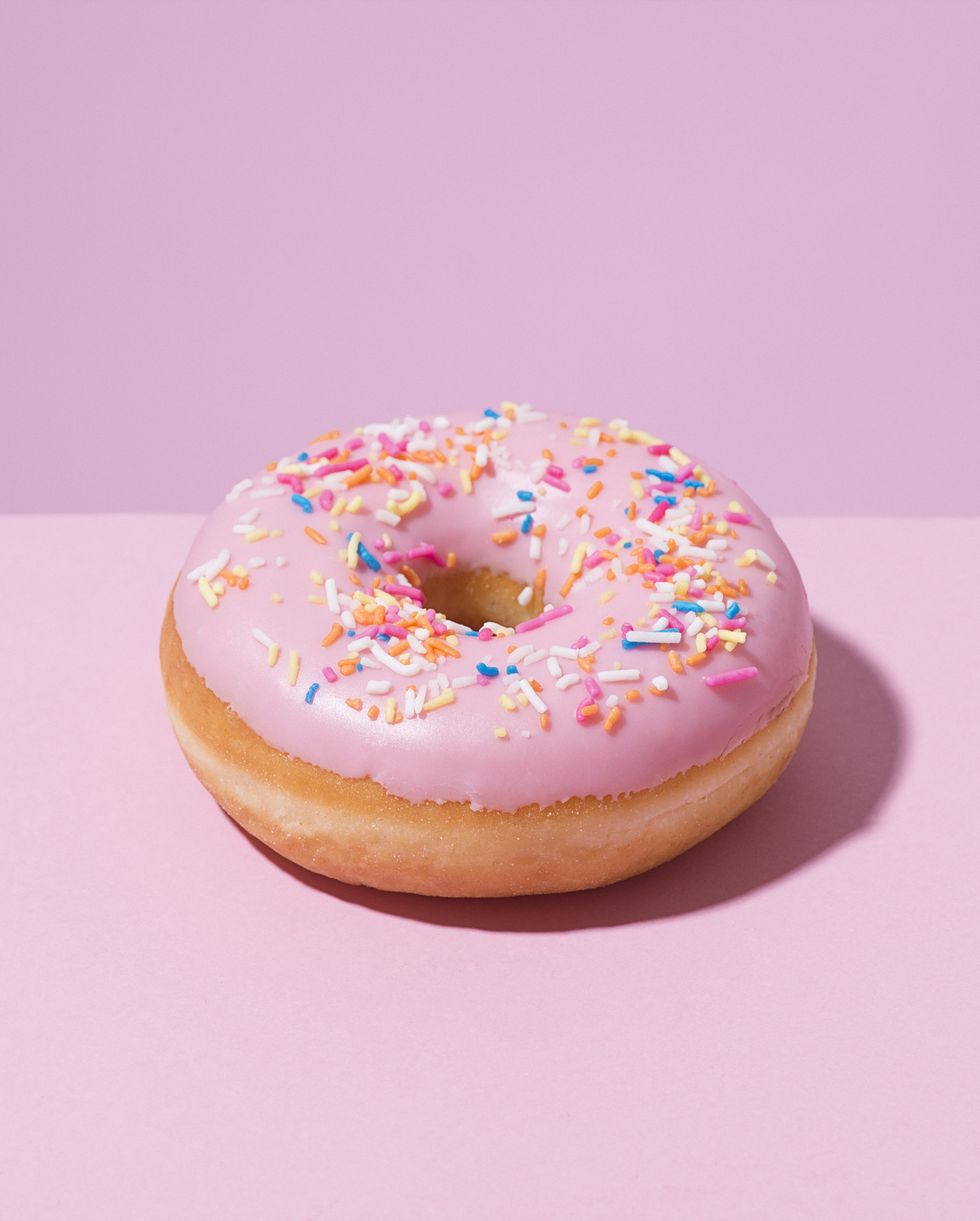 Pink doughnut with sprinkles on a pink background.