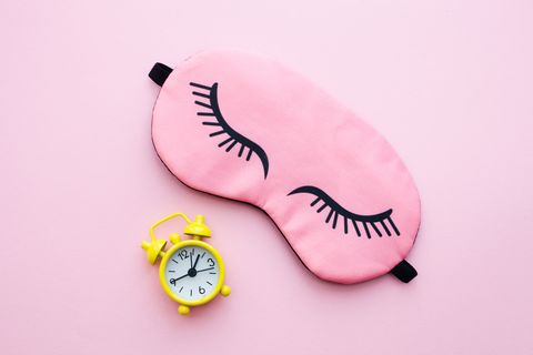 pink sleep mask and yellow alarm clock over pink background