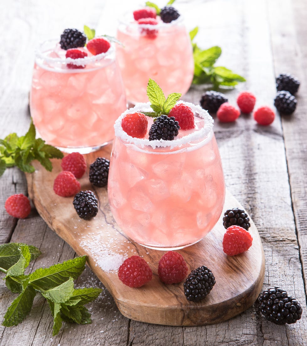 pink summer drinks with raspberries and blackberries on a wooden cutting board, good housekeeping's favorite 4th of july activities