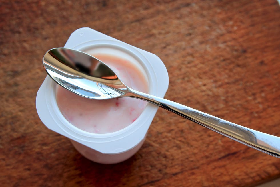 pink yogurt in plastic cup on wooden background with spoon