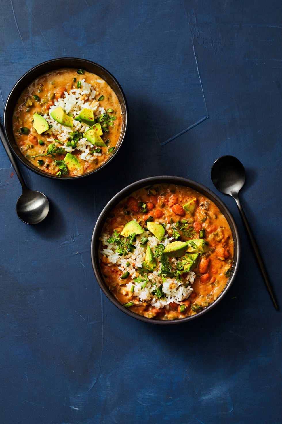 two bowls of pinto bean and poblano soup with sliced avocado on top