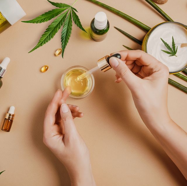 pipette with cbd cosmetic oil in female hands on a table background with cosmetics, cream with cannabis and hemp leaves, marijuana
