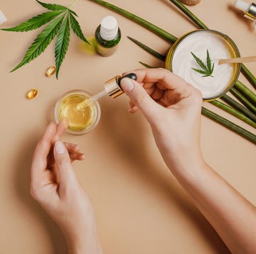 pipette with cbd cosmetic oil in female hands on a table background with cosmetics, cream with cannabis and hemp leaves, marijuana