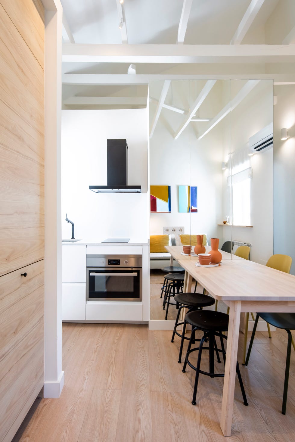 salón, comedor y cocina de diseño moderno con muebles de madera clara y pared de espejo