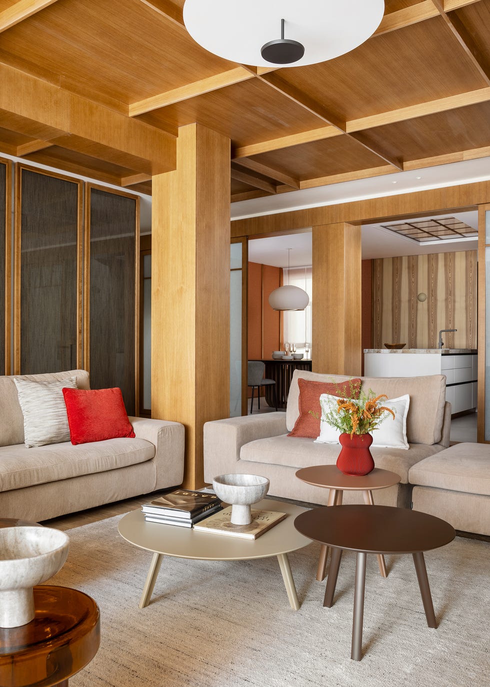 salón con techo y pilares de madera, dos sofás beige y mesas de centro tipo nido