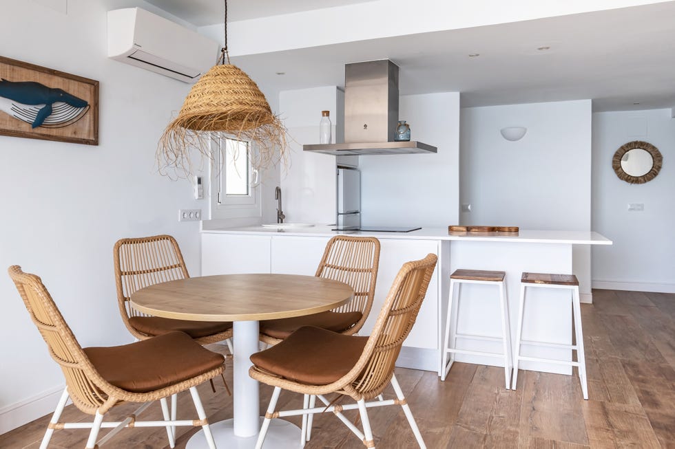 cocina blanca con península y comedor con mesa redonda de madera, sillas y lámpara de fibras