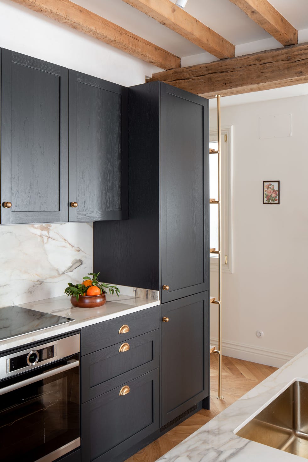 cocina con frente y encimera de mármol y armarios de madera en color negro con tiradores uñeros dorados
