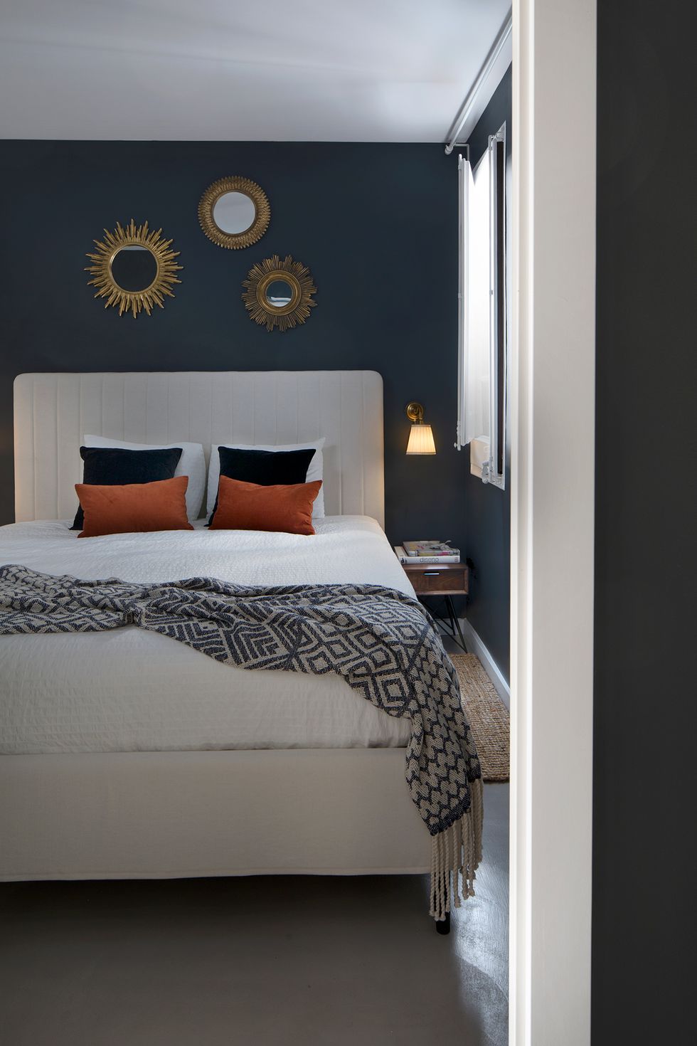 Dormitorio con cama a medida en color blanco y tres espejos tipo sol sobre el cabecero