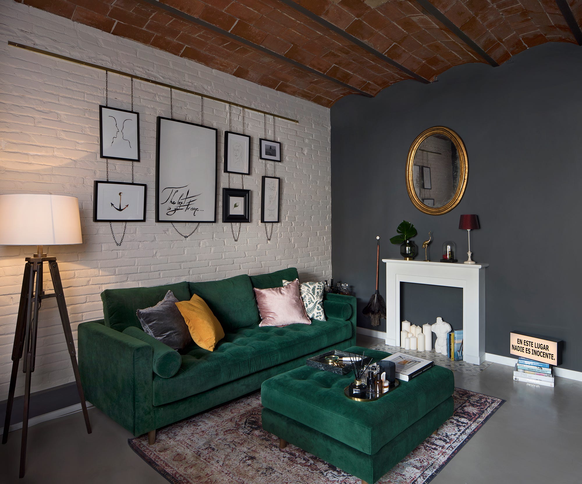 salón con paredes en gris grafito y color blanco, y un sofá de terciopelo verde con mesa de centro tipo puf a juego
