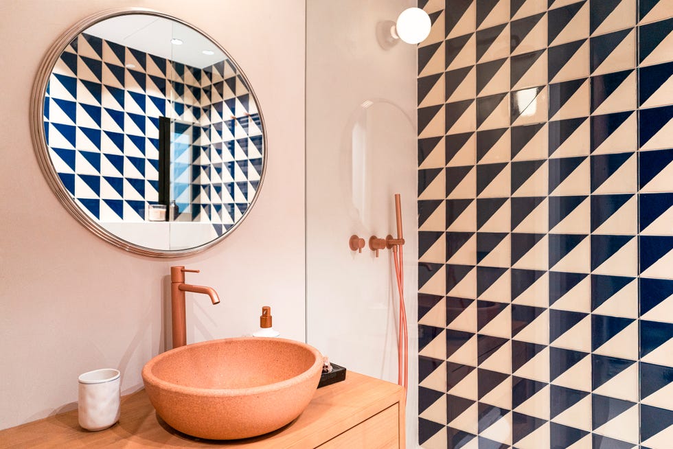 ducha revestida con azulejos geométricos y lavabo exento con grifería dorada