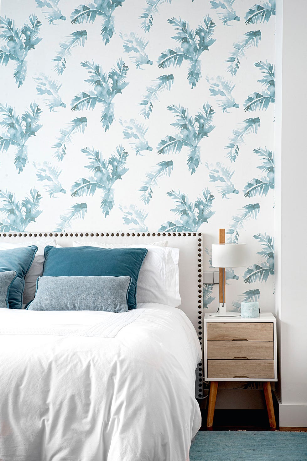 dormitorio con cabecero blanco decorado con remaches y papel pintado con hojas azules