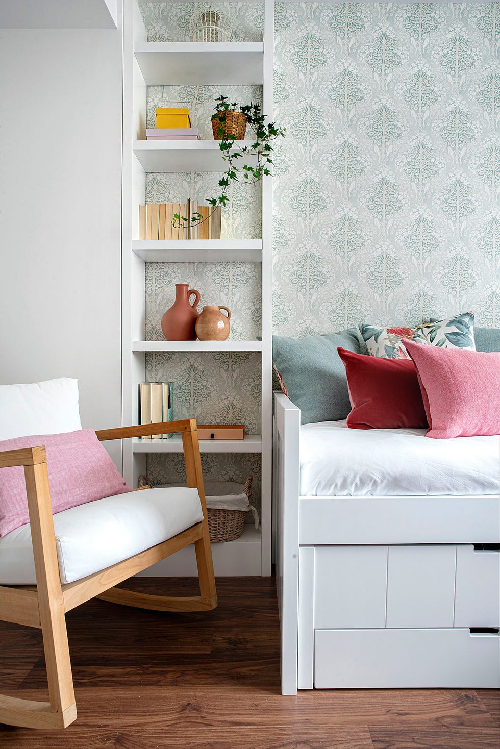 habitación con cama nido y estantería blanca, mecedora de madera y papel pintado con motivos victorianos azules