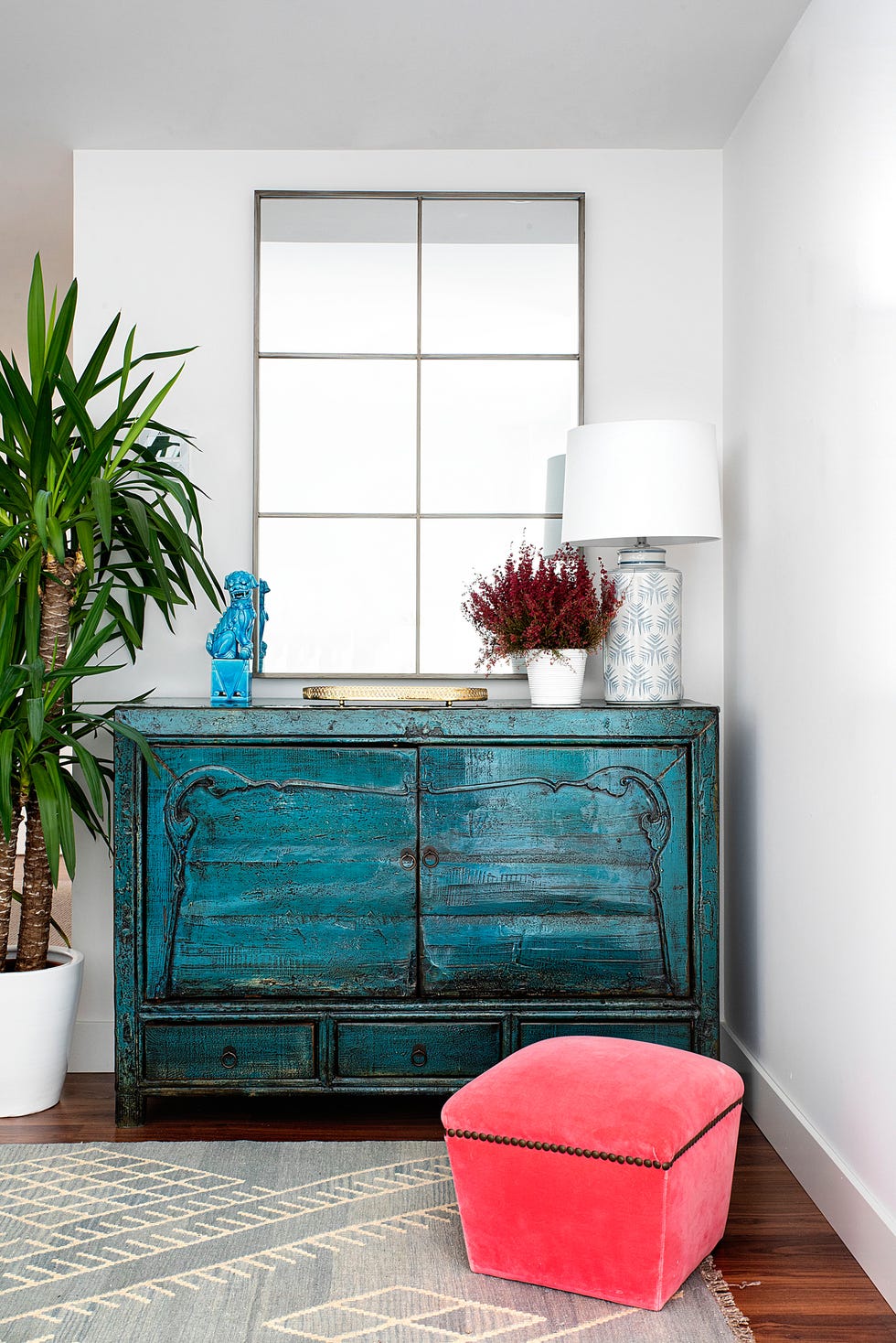 mueble antiguo pintado en azul, espejo con cuarterones y puf tapizado en terciopelo rojo