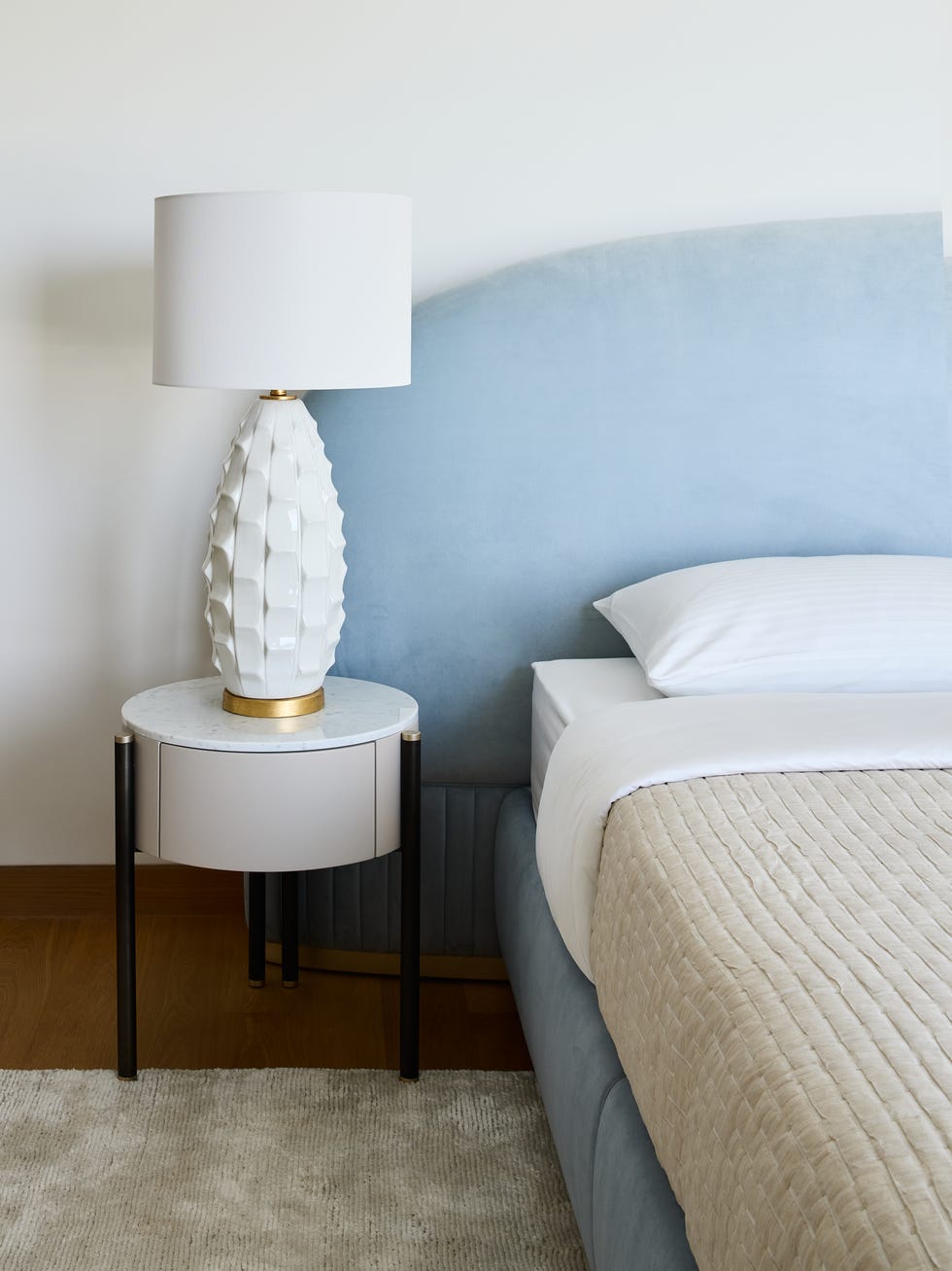 cabecero de terciopelo azul y mesita con lámpara de mesa blanca