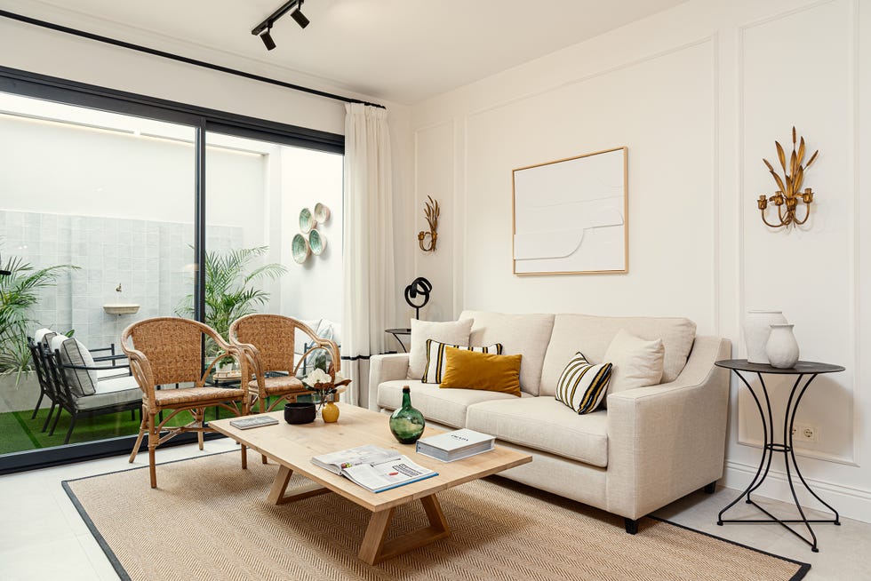 sofá beige, mesa de madera, butacas de ratán y pared con molduras