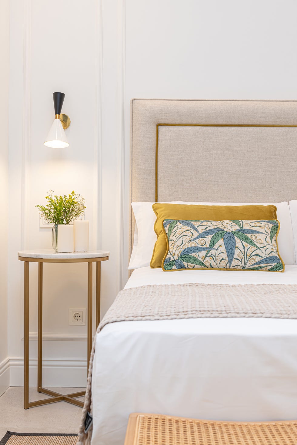 cama con cabecero tapizado en beige, mesita de mármol y latón y pared con molduras
