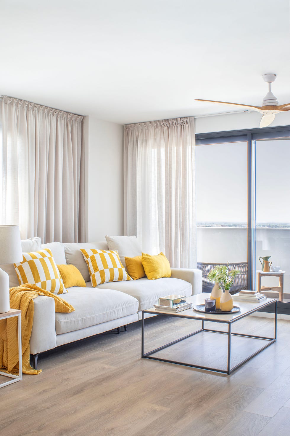 salón con sofá gris con textiles amarillos y mesa de centro de acero y madera