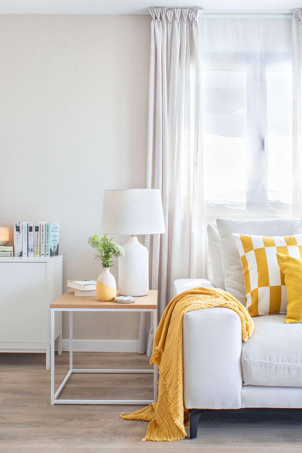 sofá gris con textiles amarillos y mesa auxiliar de madera y metal blanco